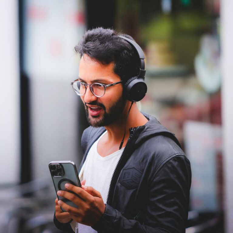 Young man with headphones holding a smartphone, engaged in conversation outdoors.